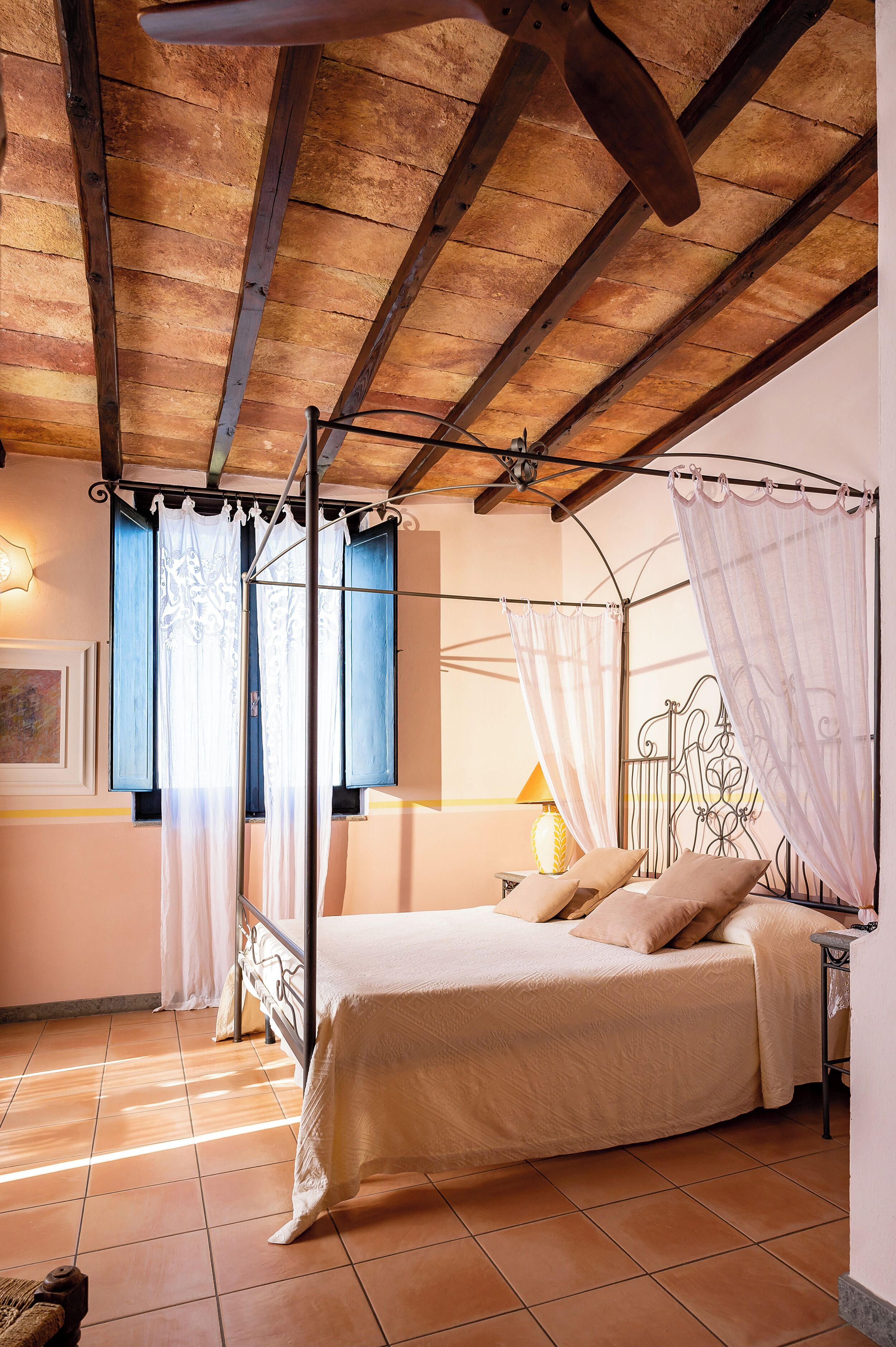 A bedroom with a four-poster bed, a nightstand, a lamp, and a window with curtains.
