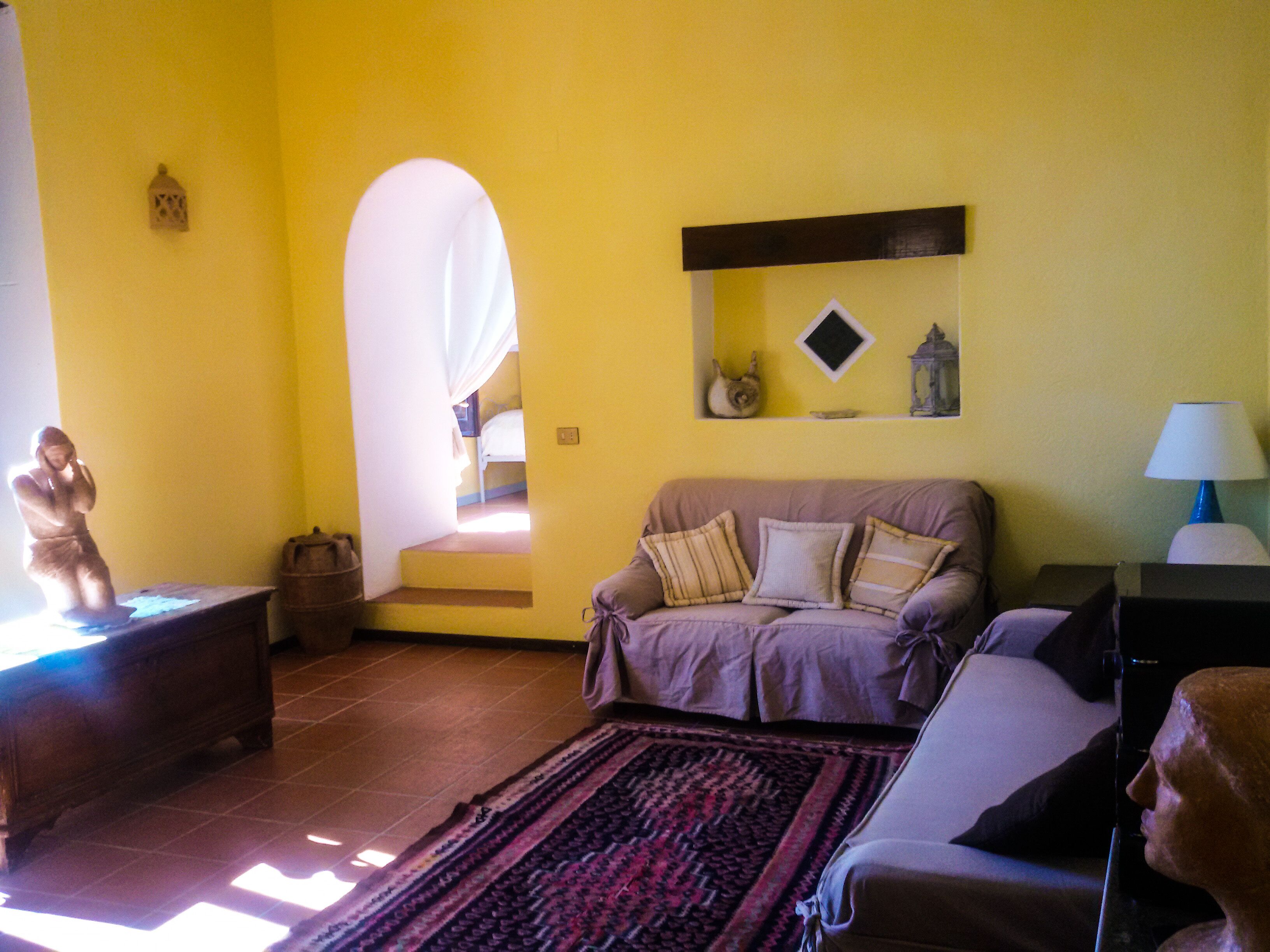 A living room with a sofa, a statue, a rug, and a staircase leading to a bedroom.