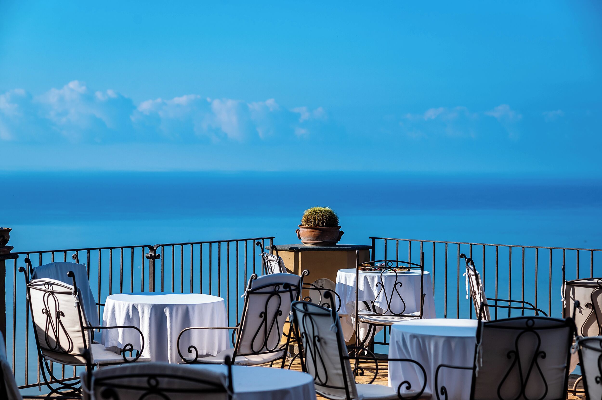 Une terrasse avec des tables et des chaises, un pot de fleurs et une vue sur la mer.