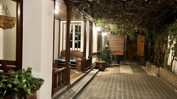 A narrow brick pathway leading to a wooden building with a covered seating area. - Gorilla - Hostel (Mendoza)
