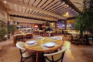 Un restaurante con mesas y sillas de madera, una zona de bar y un ventanal con vistas.