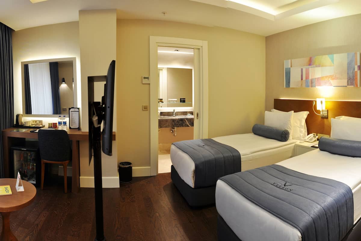 Una habitación de hotel con dos camas, un escritorio, una silla, una mesita y un televisor.