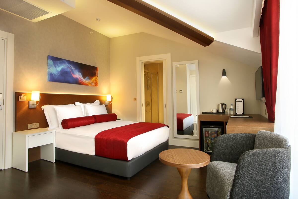Una habitación de hotel con cama, mesita de noche, silla y una pequeña mesa redonda.