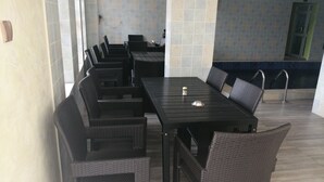 A dining area with a long table and multiple chairs, a tiled wall, and a pool in the background. - GrandVenice Transit Apartments (Lagos)