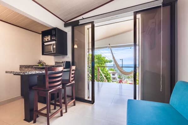A modern kitchen with a bar area, a blue sofa, and a view of the ocean through large sliding doors. - Villas de la Selva (Quepos)