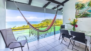 Un balcon agrémenté d’un hamac, de chaises, d’une table et d’un tableau représentant un paysage tropical.