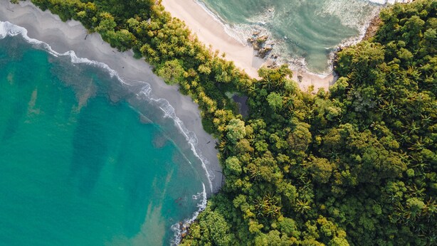 Vue aérienne d’une zone côtière avec une plage, une végétation luxuriante et des eaux turquoise cristallines.