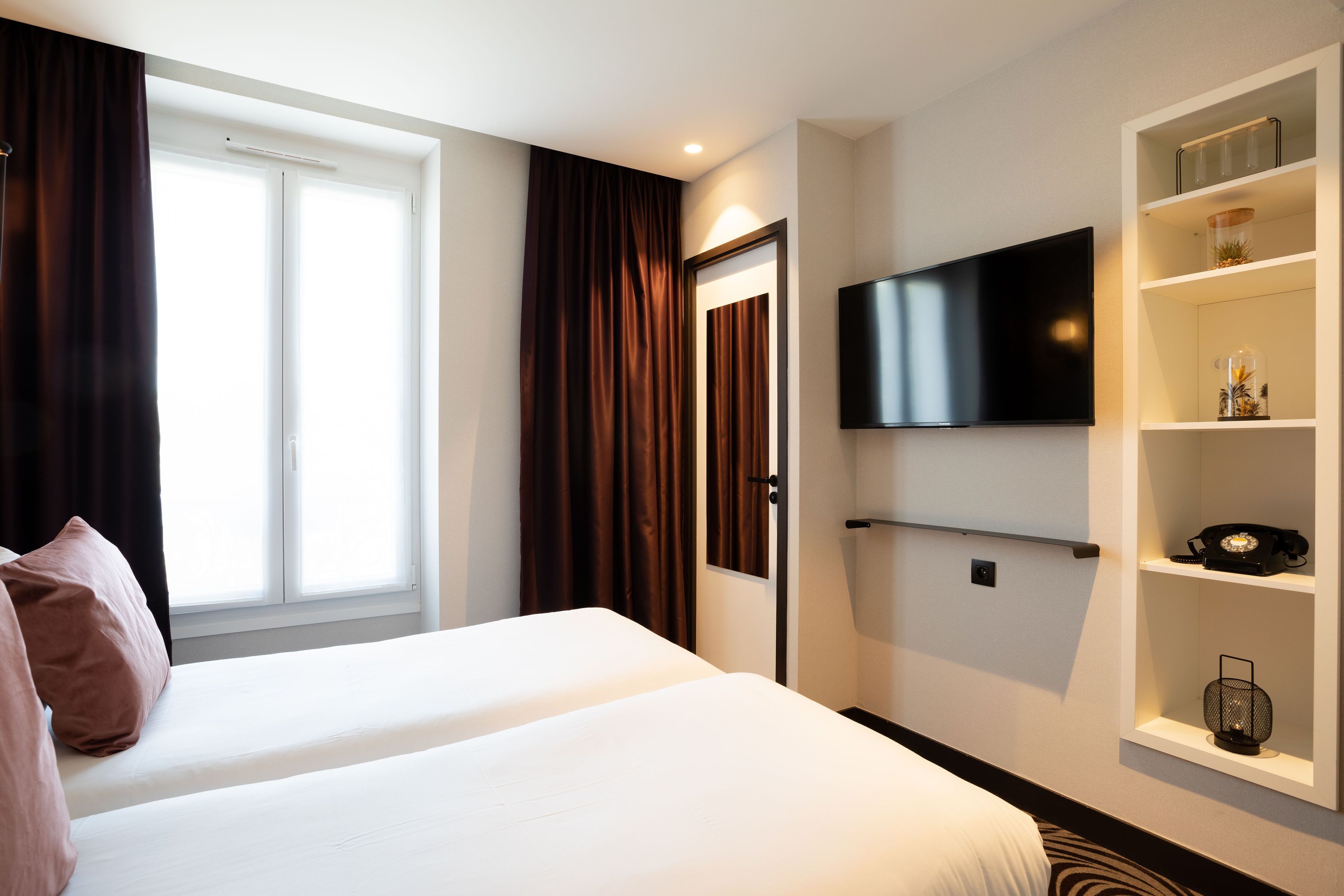 A hotel room with a bed, a television mounted on the wall, and a shelf with decorative items.