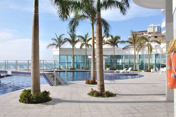A pool area with palm trees, lounge chairs, and a lifebuoy. - Apartamentos frente al mar Cartagena - Edificio Palmetto (Cartagena)