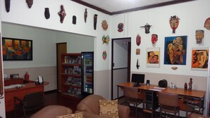 A living room with a sofa, a desk, and a bookshelf. There are various masks and paintings on the walls. - Hotel Santamaria (Alajuela)