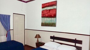 A hotel room with a bed, two blue chairs, a nightstand with a lamp, and a door. - Hotel Santamaria (Alajuela)