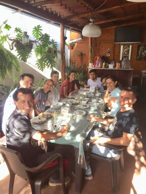 A group of people dining at an outdoor table with a checkered tablecloth, surrounded by plants and wooden beams. - Hotel Santamaria (Alajuela)