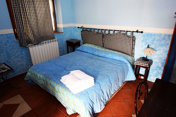 A bedroom with a blue bedspread, a checkered headboard, a small bedside table, and a radiator. - B&B Giucalem - La Casa Negli Orti (Piazza Armerina)