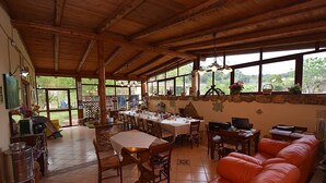 Un vaste espace dédié à la salle à manger, avec une longue table en bois et des chaises, une table à manger recouverte d’une nappe blanche, et un grand canapé en cuir orange.