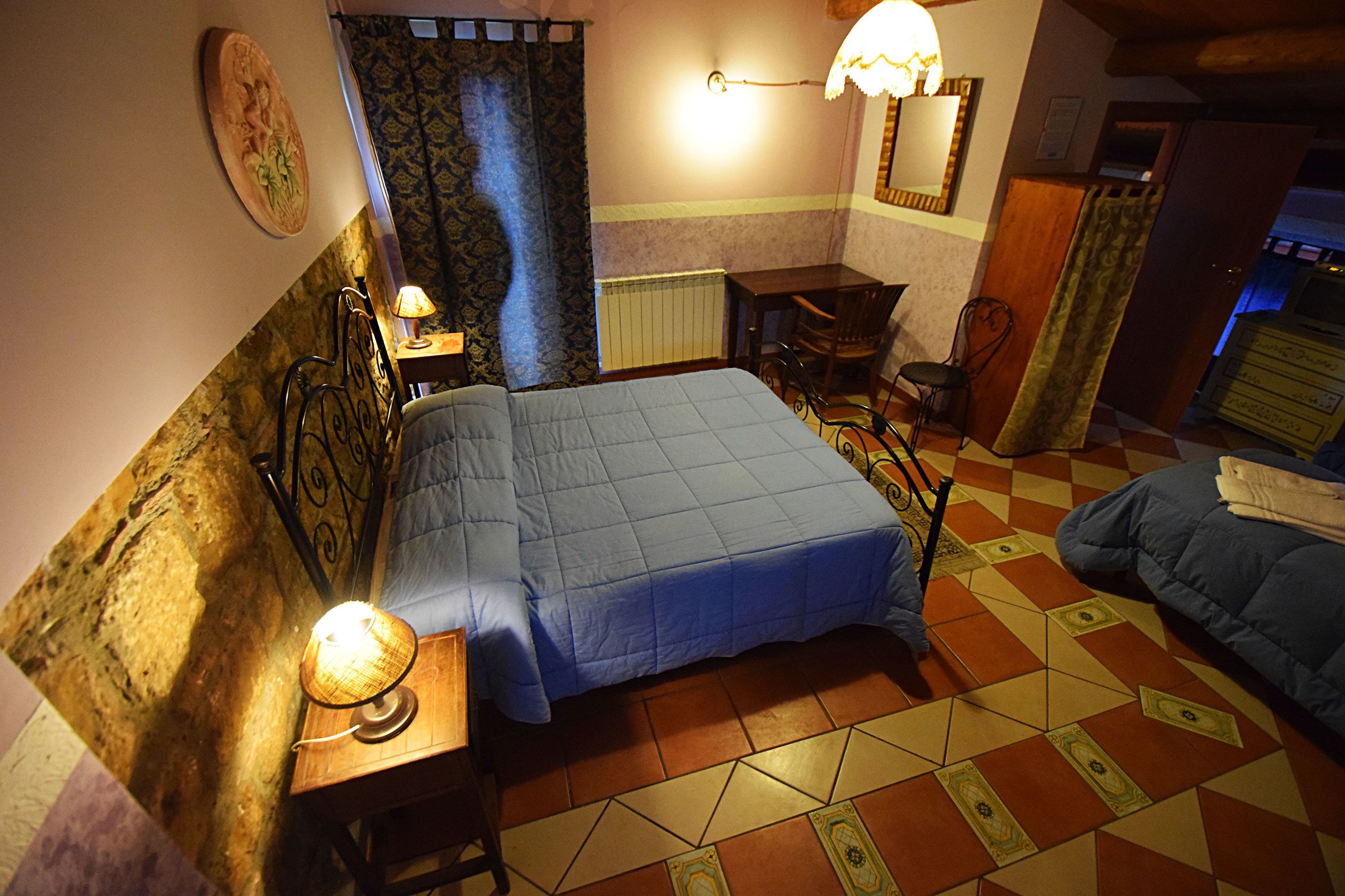 Una habitación con una cama, un escritorio y una silla. Hay una lámpara en el escritorio y una ventana con cortinas.