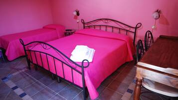 Une chambre avec deux lits, chacun recouvert d’une couvre-lit rose et doté d’un cadre en métal noir. On y trouve une table en bois avec une chaise, ainsi qu’une petite table ronde avec une lampe.