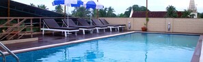 A swimming pool with lounge chairs and umbrellas, surrounded by a wooden deck and a brick wall.