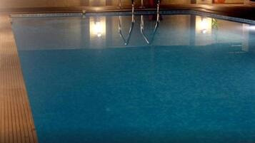 Una piscina con agua cristalina, un muelle de madera y escaleras de metal.