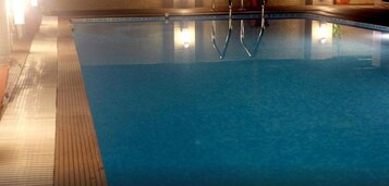 Una piscina con agua cristalina, un muelle de madera y escaleras de metal.