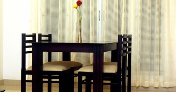 A dark wooden table with two cushioned chairs in a room with light-colored curtains.