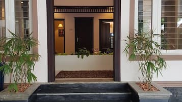 A building entrance with a dark wooden door, steps leading up to a landing, and potted plants on either side.