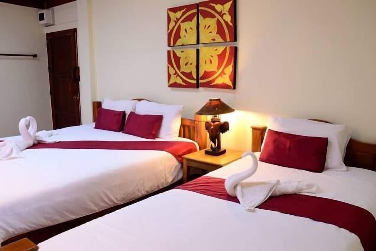 A hotel room with two beds, each with white linens and red accents, a wall-mounted artwork, and a bedside lamp.