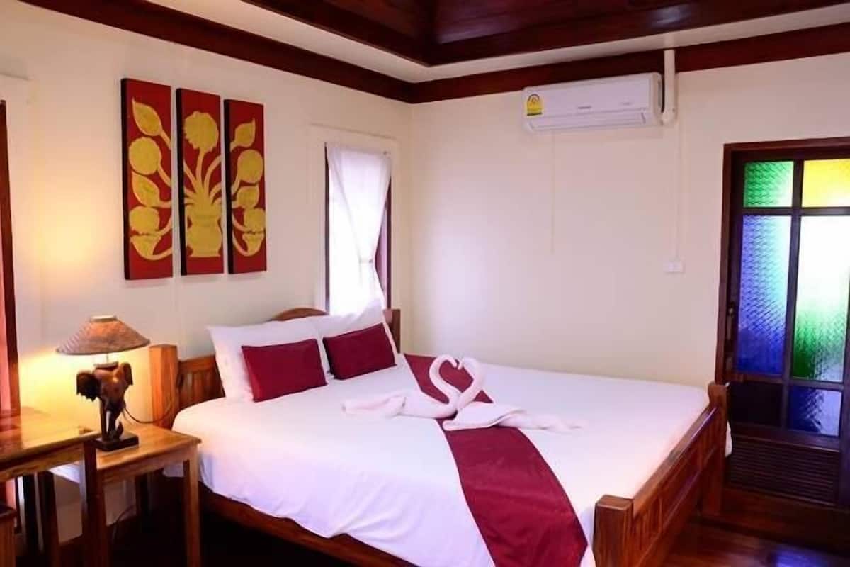 A neatly made bed with a red and white bedspread, a pair of white towels, and a decorative lamp on a wooden bedside table.