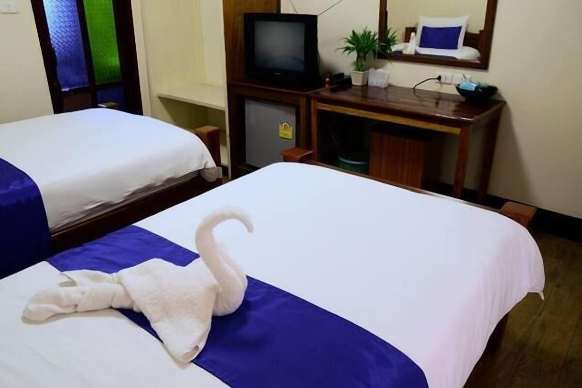 A hotel room with two beds, a television, a small refrigerator, and a desk with a plant.