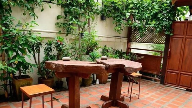 A patio area with wooden tables and chairs, surrounded by potted plants and a wooden gate. - Huenchandee (Chiang Rai)