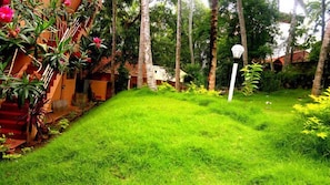 A lush green garden with a white lamp post, surrounded by tall trees and various plants.