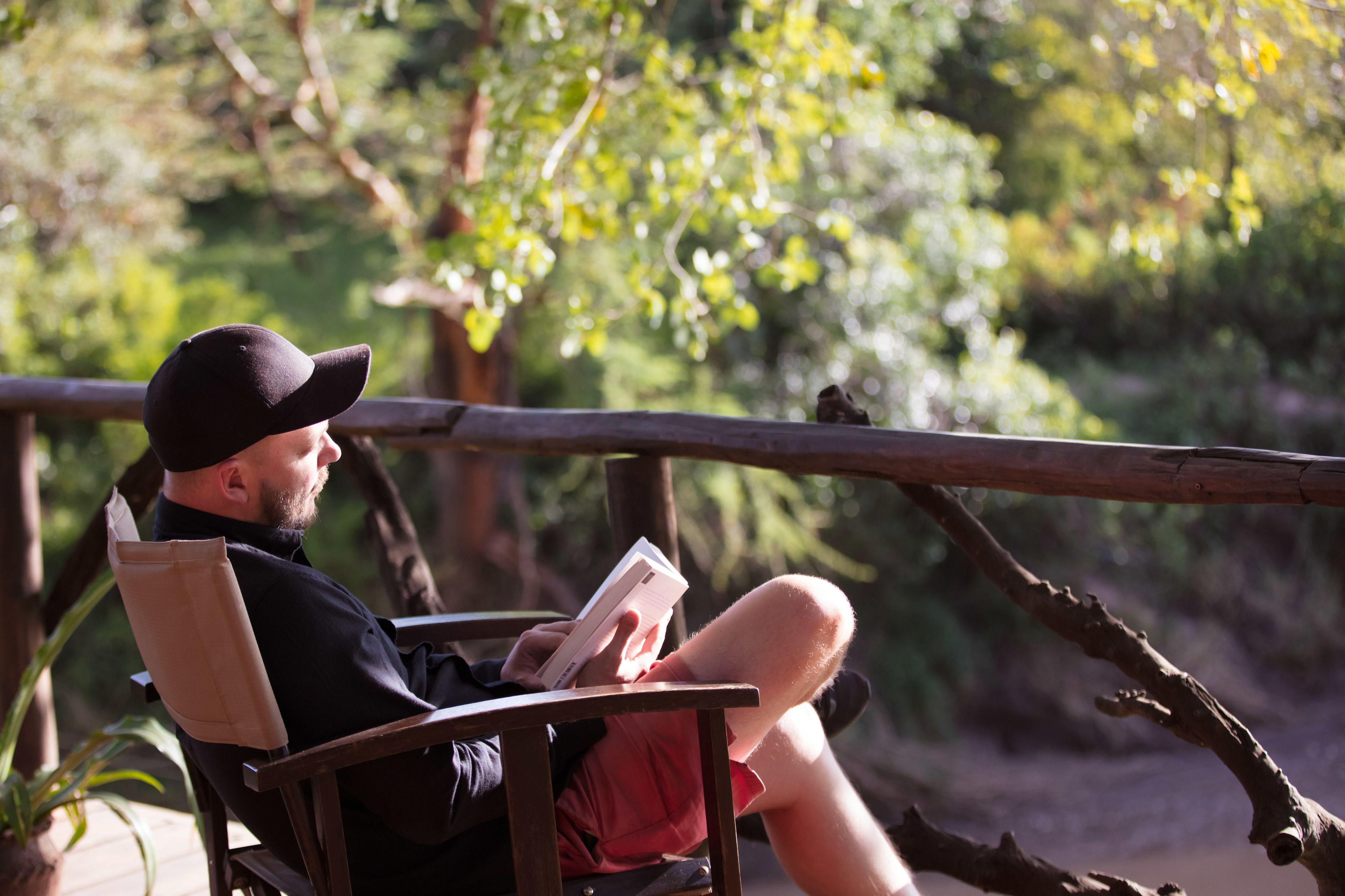 A person sitting on a wooden chair outdoors, reading a book.