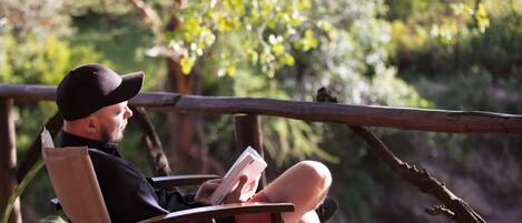 A person sitting on a wooden chair outdoors, reading a book.