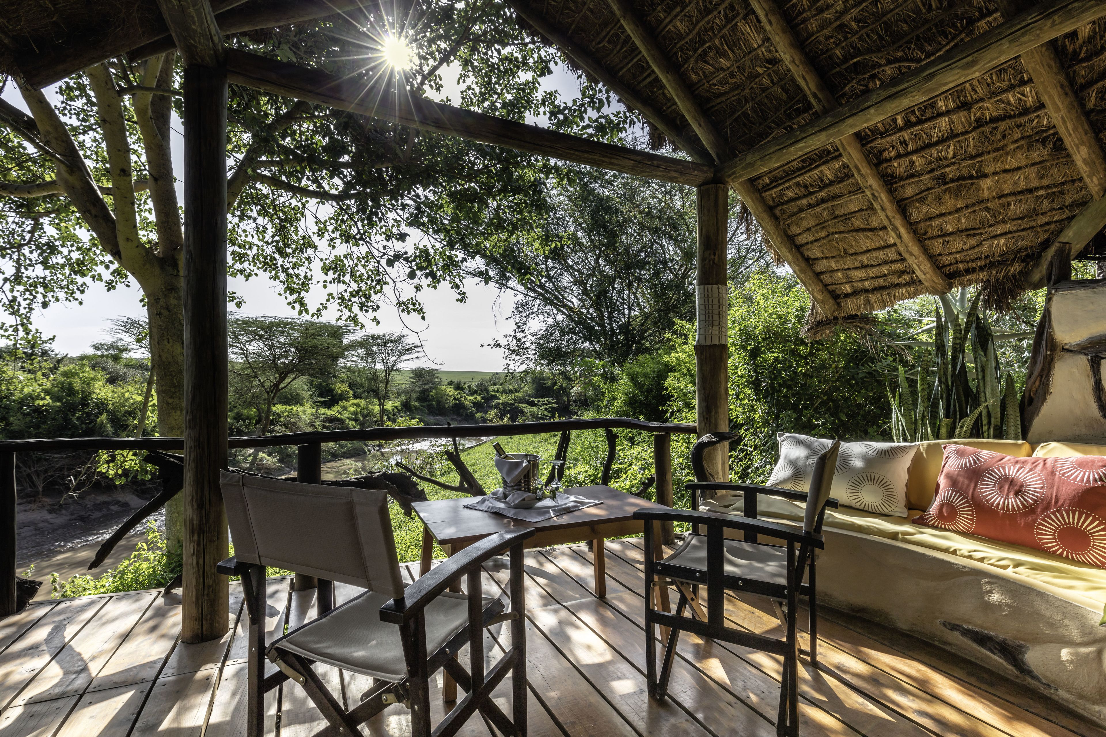 An outdoor wooden deck with a thatched roof, a sofa, and a table with chairs.