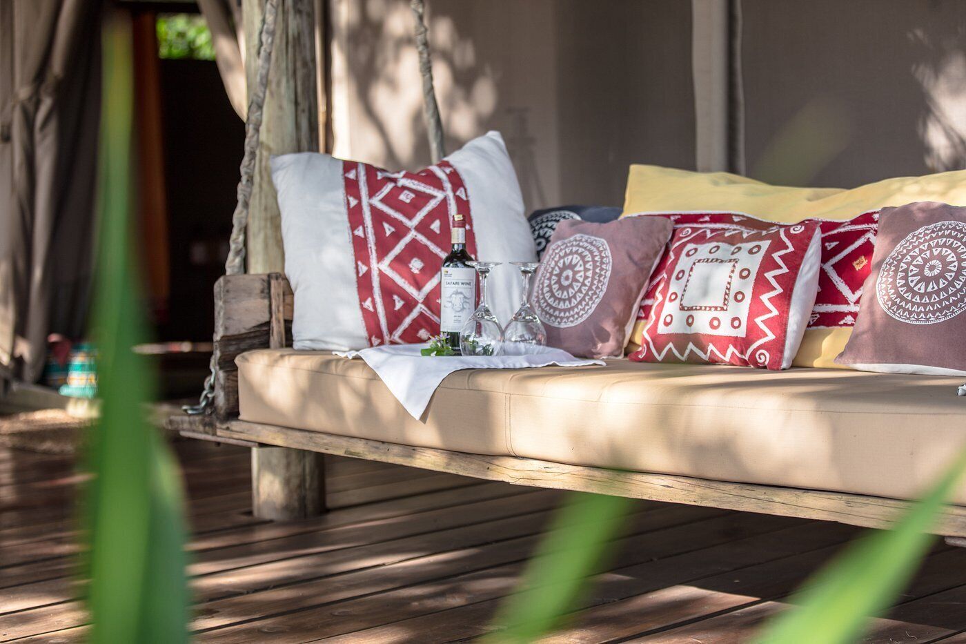 A wooden bench with cushions and a bottle of wine, set on a wooden deck.