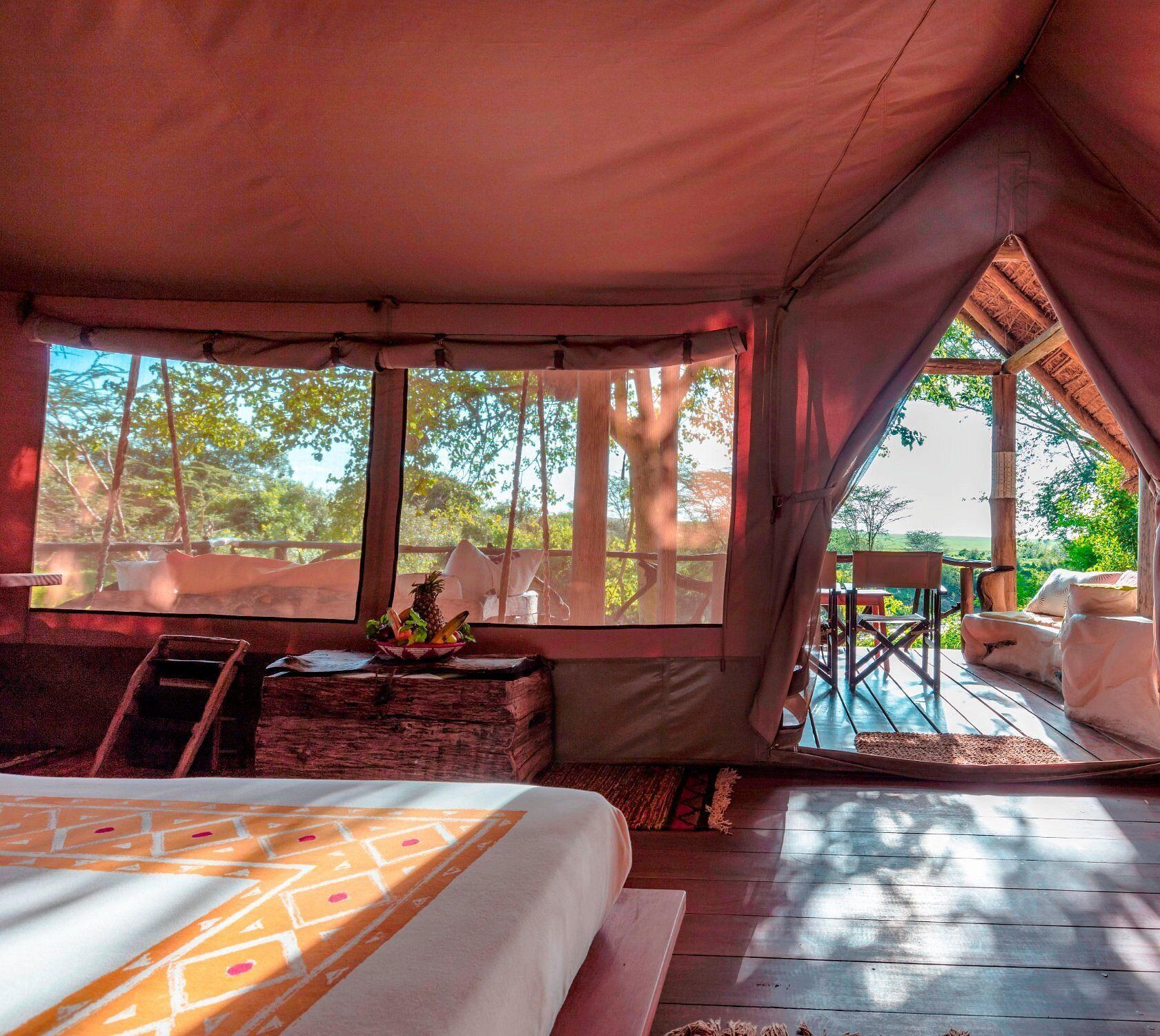 A tented accommodation with a bed, a small table with a fruit bowl, and a view of the outdoors.