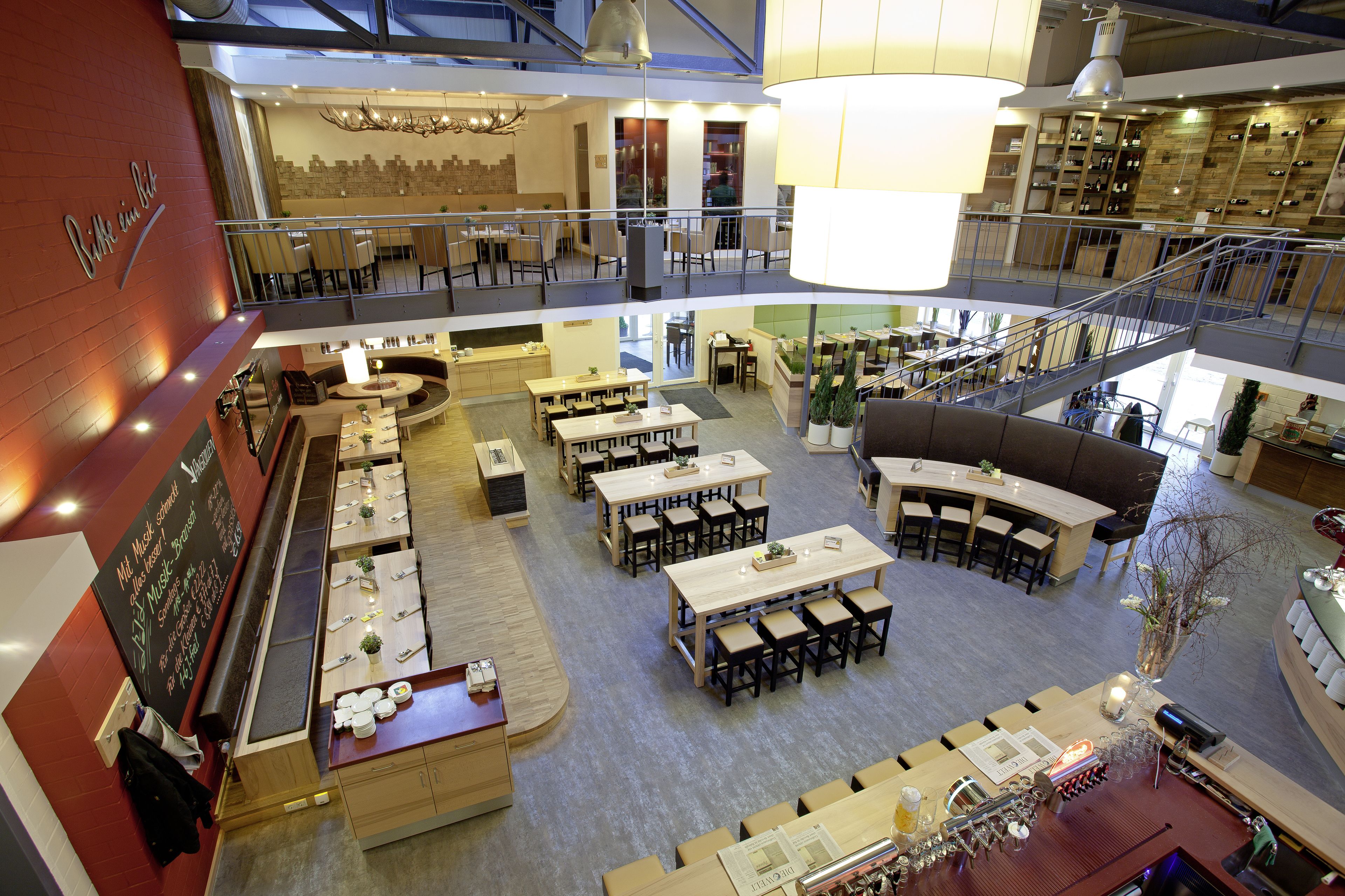 A multi-level restaurant with various seating arrangements, including tables and booths, and a bar area with a wine rack.