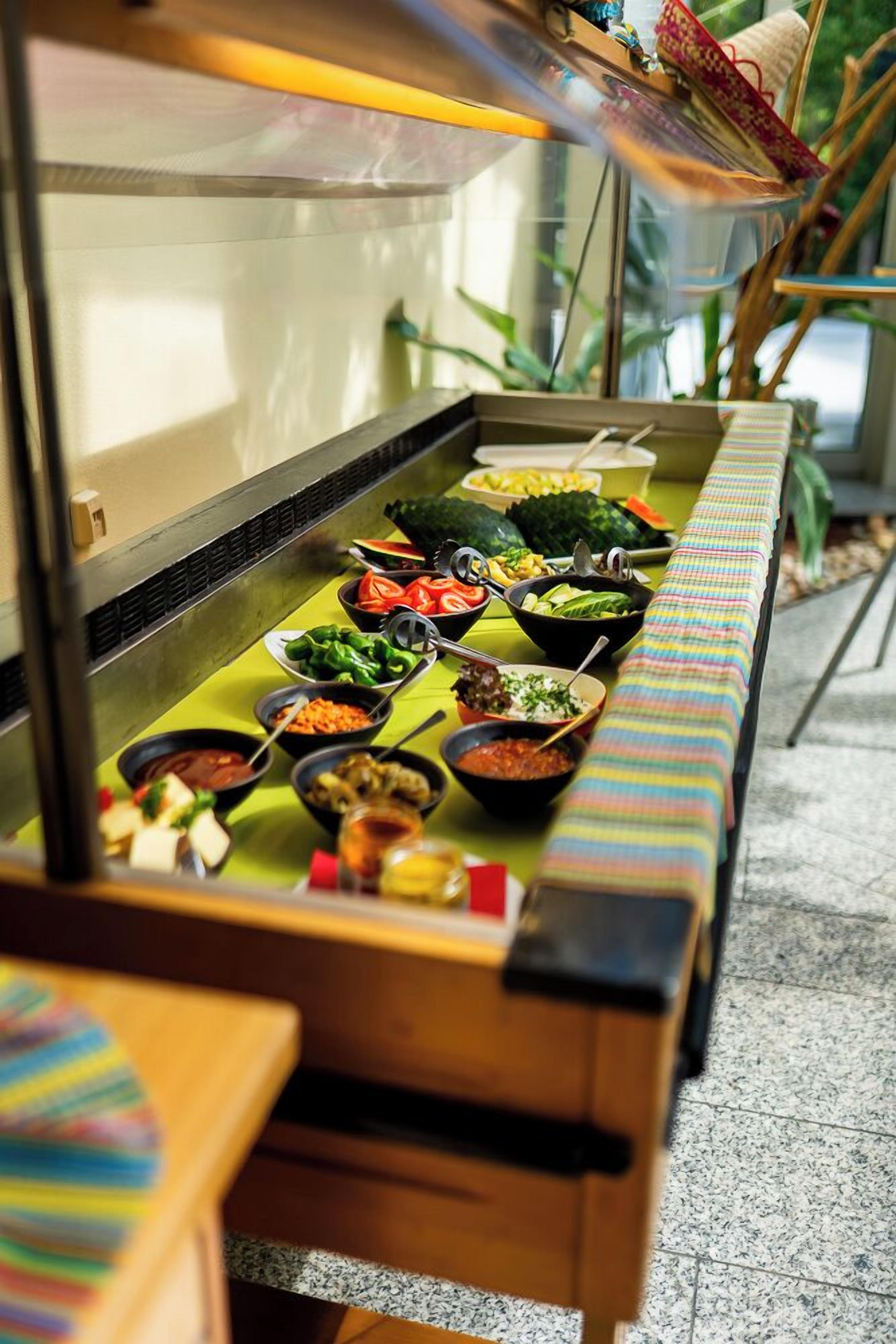 A buffet with various dishes and a long table with a colorful tablecloth.