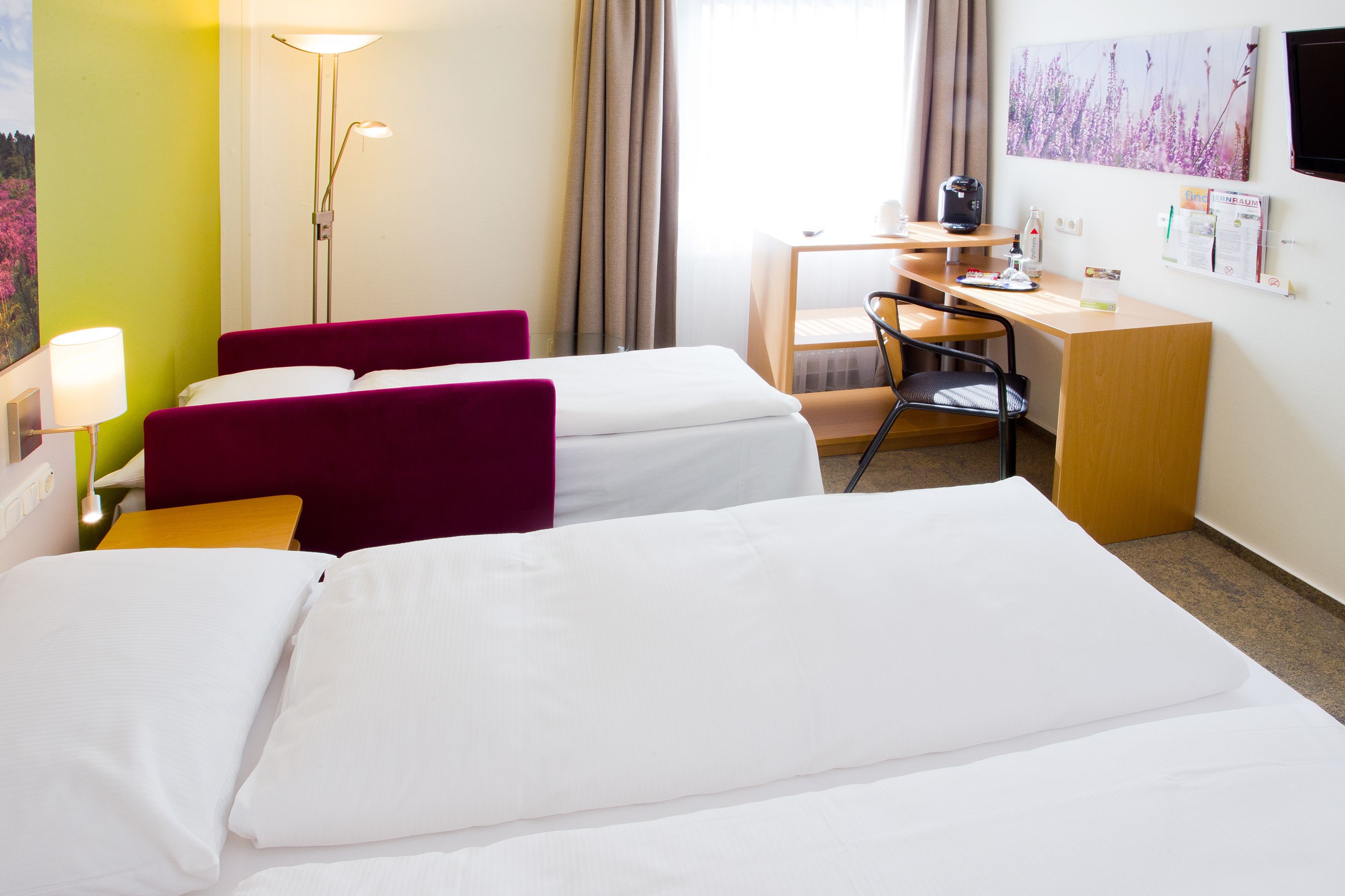 Habitación de hotel con dos camas, un escritorio, una silla, una lámpara y una ventana con cortinas.
