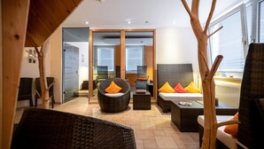 Una habitación moderna y luminosa con mobiliario de mimbre, un adorno de madera con forma de árbol y vistas a otra habitación a través de un ventanal.