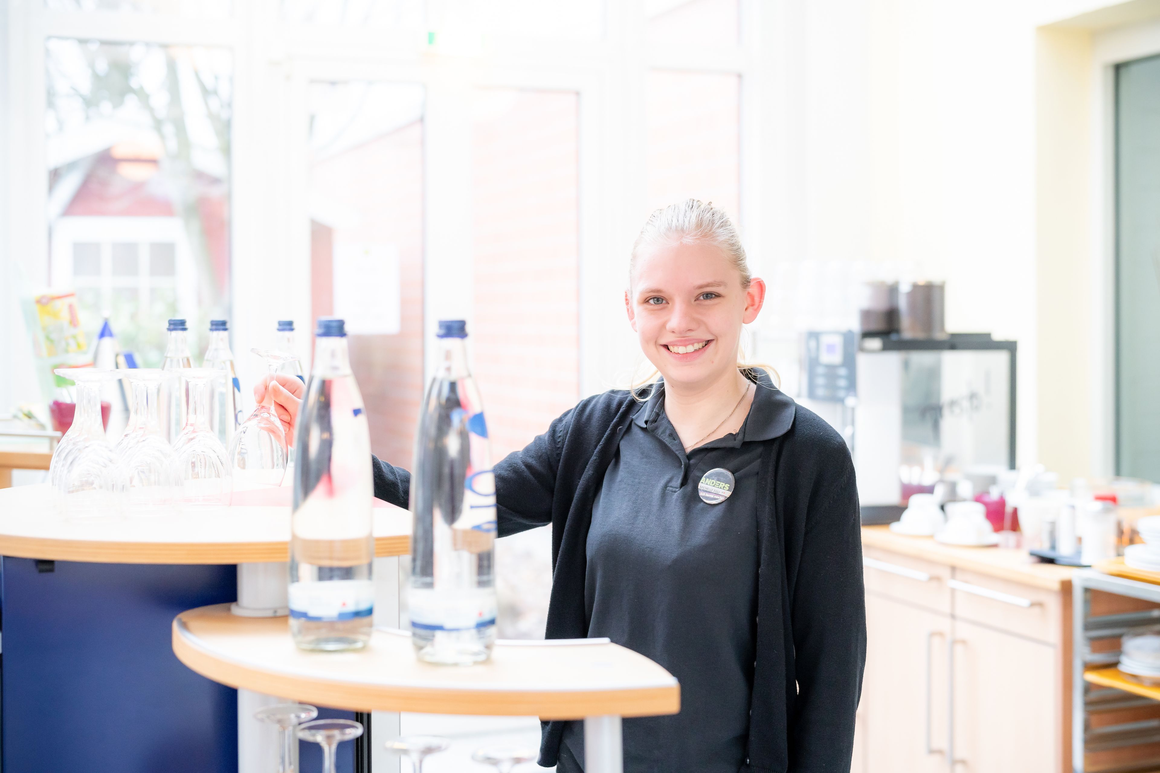 A person standing at a counter with water bottles and glasses.