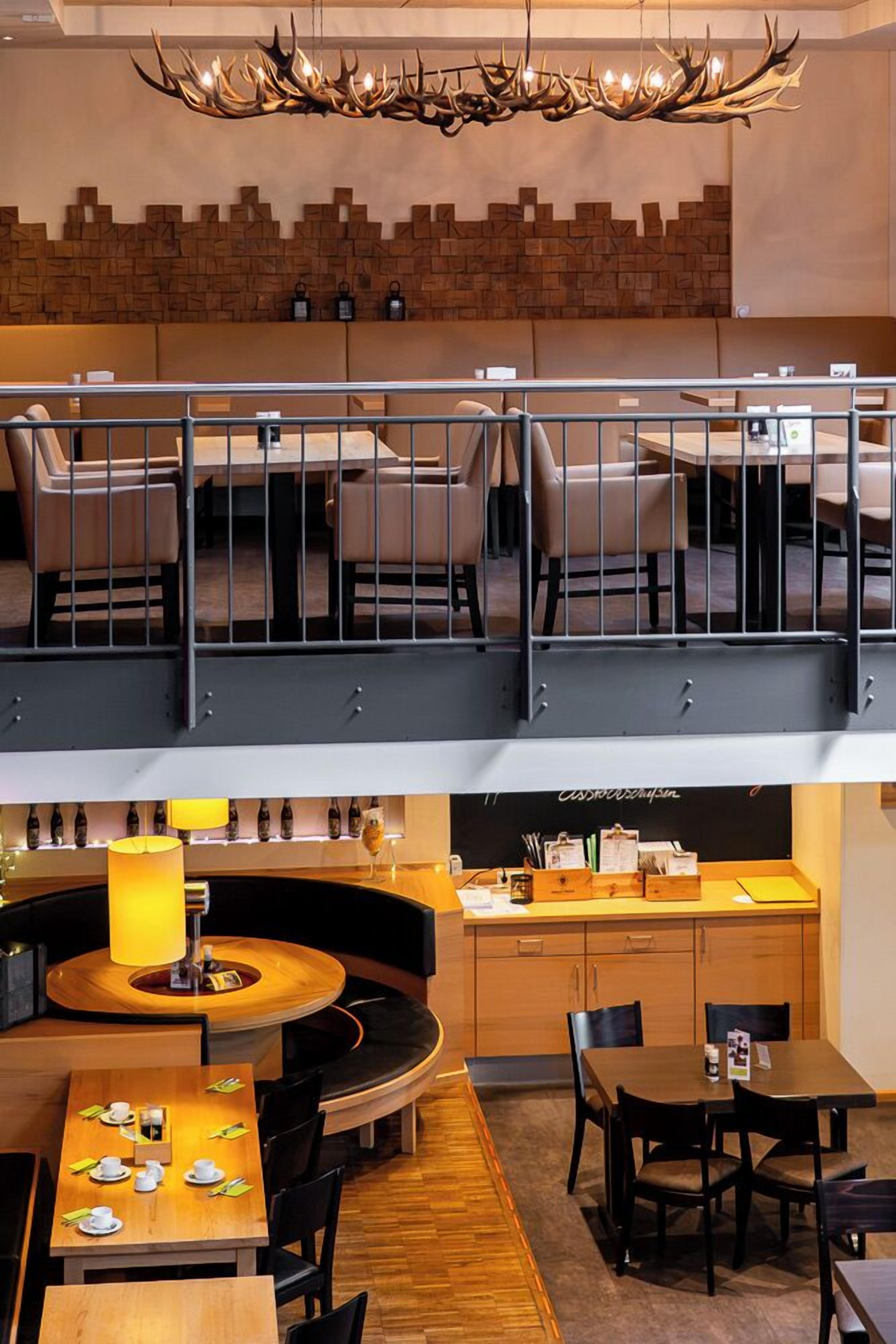 A restaurant with a high ceiling, a unique antler chandelier, and a brick wall design.