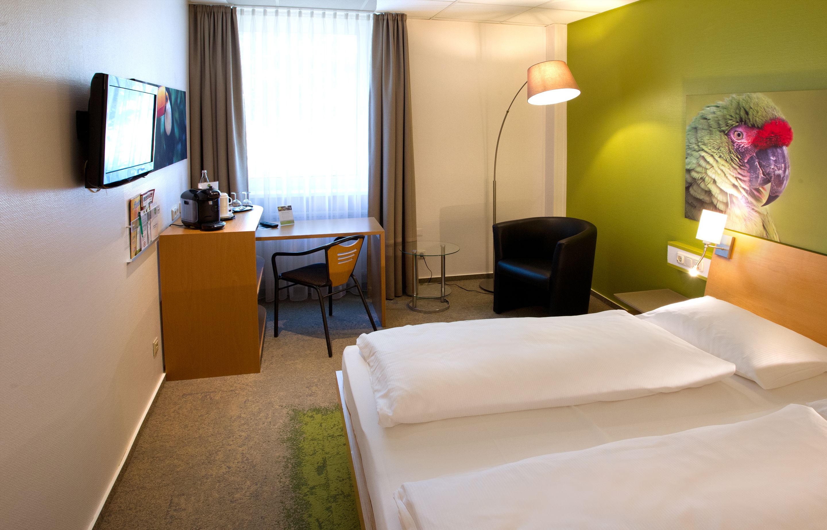 Habitación de hotel con cama, escritorio, silla y televisión en la pared.