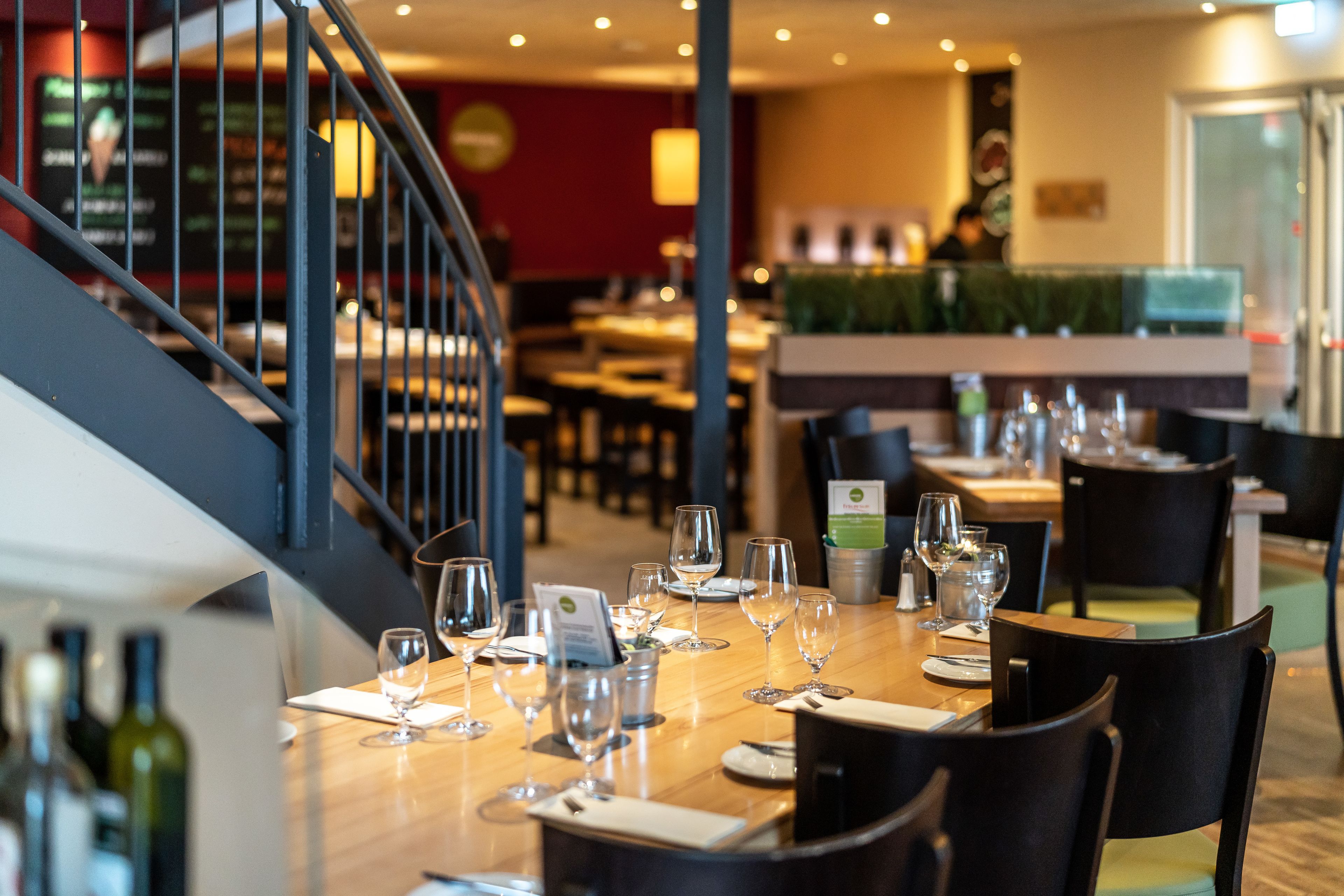 Un restaurante con mesas preparadas para comer, una escalera y una zona de bar.
