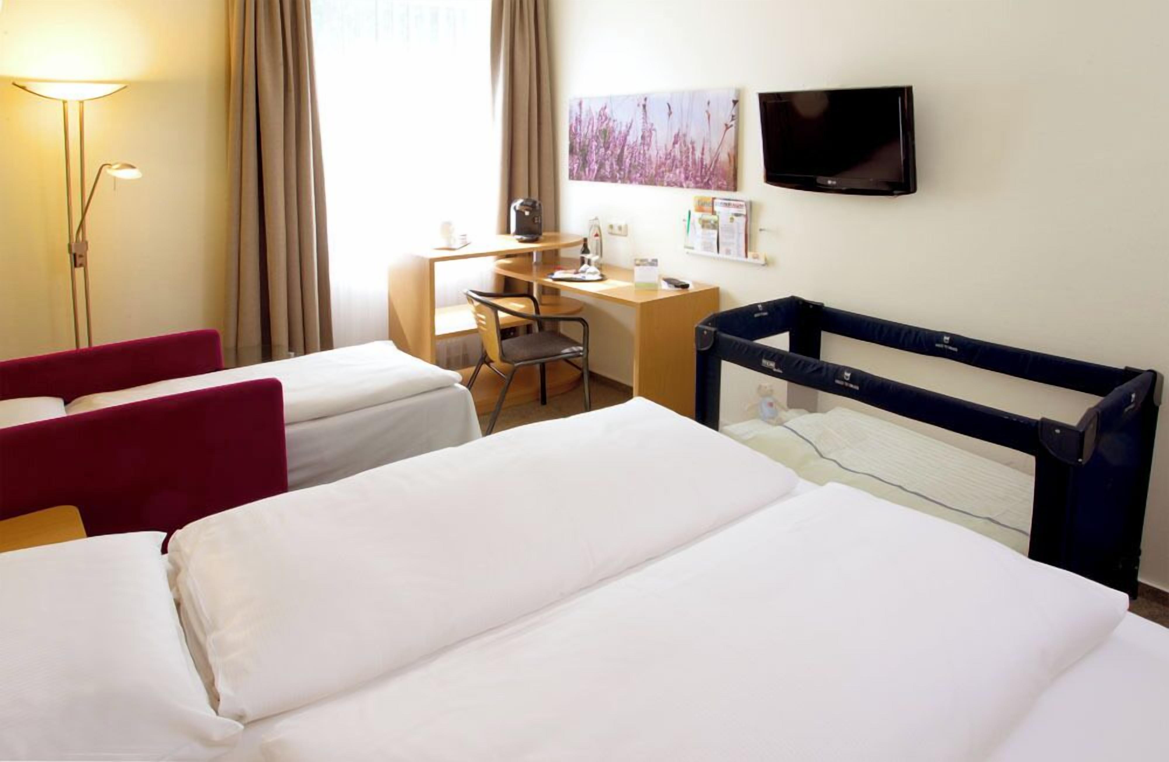 A hotel room with two beds, a desk, a chair, a TV, and a window with curtains.