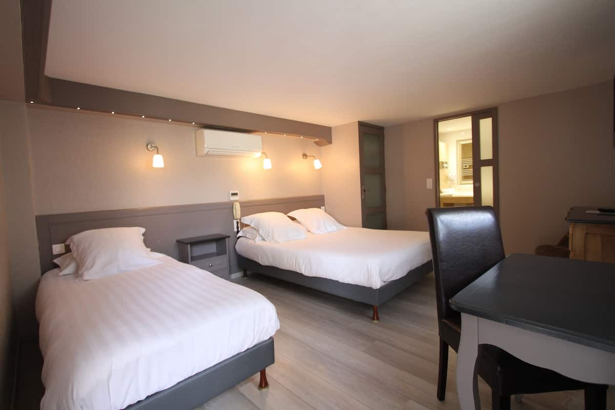 A hotel room with two beds, a desk, and a chair. There is a mirror on the wall and a door leading to another room.
