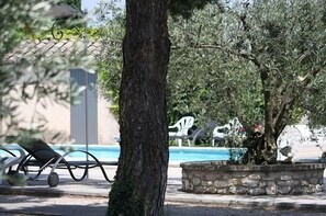 A poolside area with a stone planter, lounge chairs, and a tree. - Hotel Van Gogh (St.-Rémy-de-Provence)