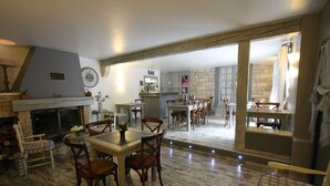 A spacious living area with a fireplace, dining table, and chairs. There is a kitchen area with a bar and a stone wall. - Hotel Van Gogh (St.-Rémy-de-Provence)