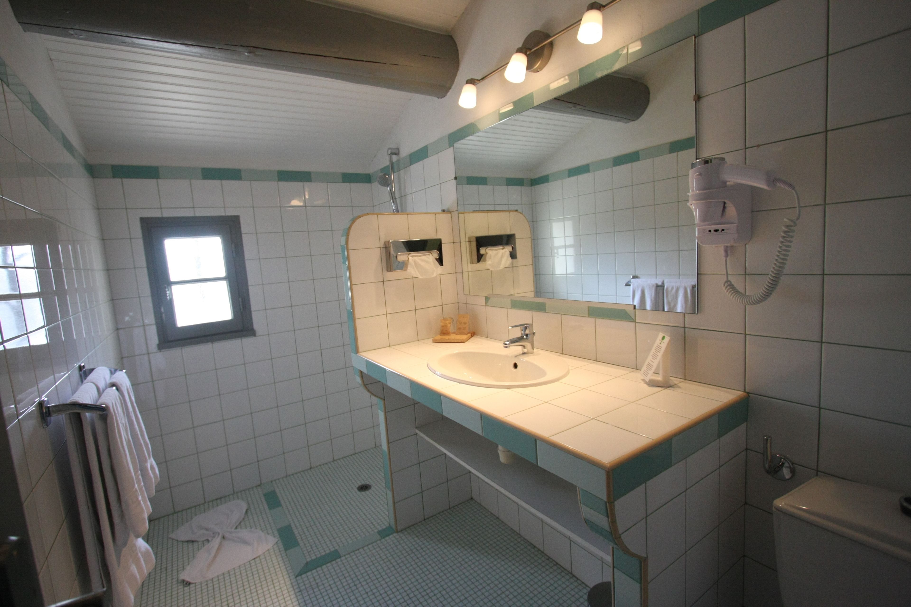 Ein Badezimmer mit Waschbecken, Spiegel, Handtuchhalter und einem an der Wand befestigten Föhn.