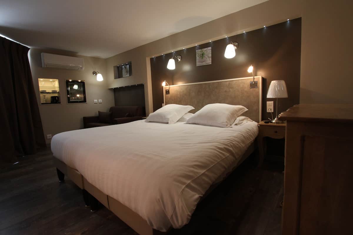 A hotel room with a large bed, bedside tables, a lamp, and wall-mounted lights.