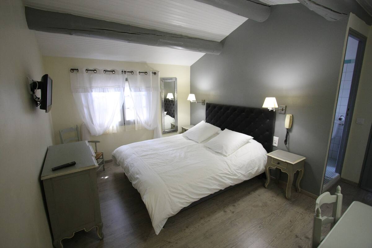 A bedroom with a large bed, bedside tables, a mirror, and a television on a stand.